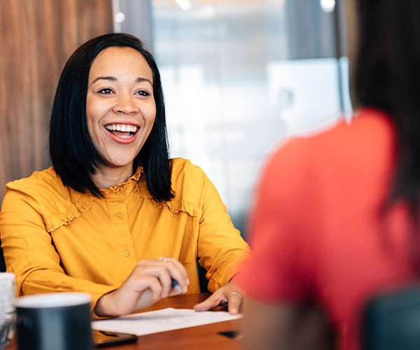 Woman smiling and sitting across the table from someone 