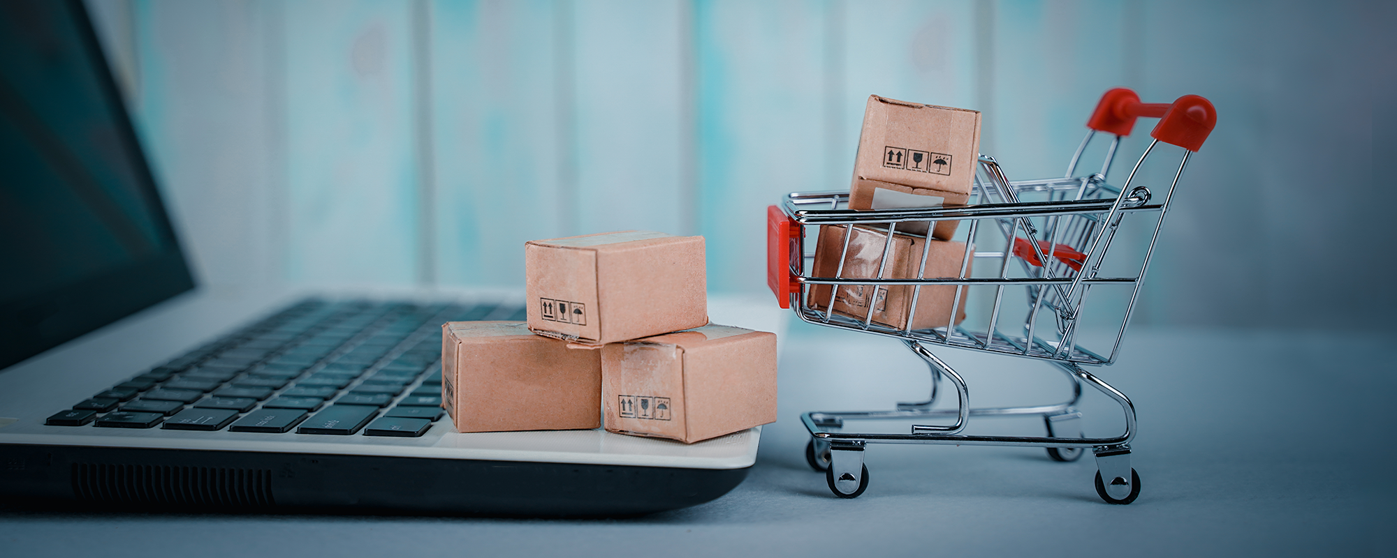 photo of a mini shopping cart filled with brown packages next to a laptop (banner image)