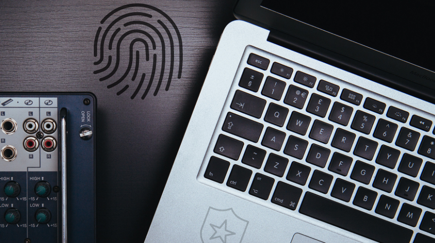 A laptop, audio equipment, a black fingerprint all scattered on top of a desk.