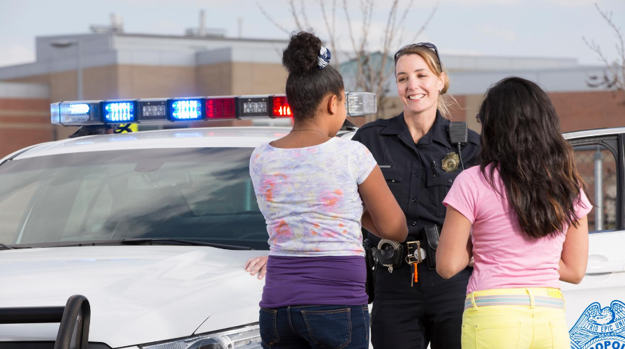 A female police officer talking to two young students outside of a school.