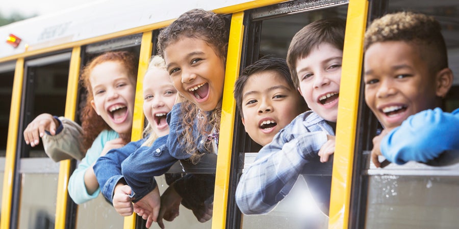 Elementary school children smiling out of school bus windows