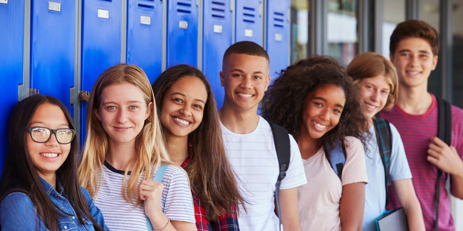 Group of students smiling and standing in front of lockers