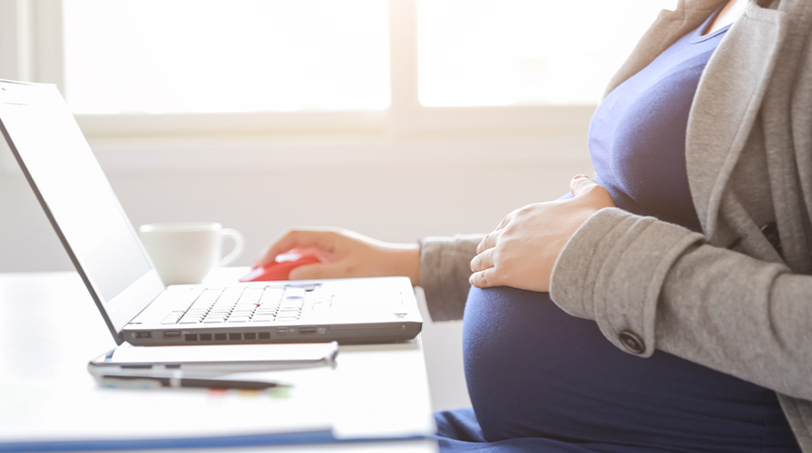 photo of a pregnant woman with left hand on her belly and right hand on a mouse, working at her laptop