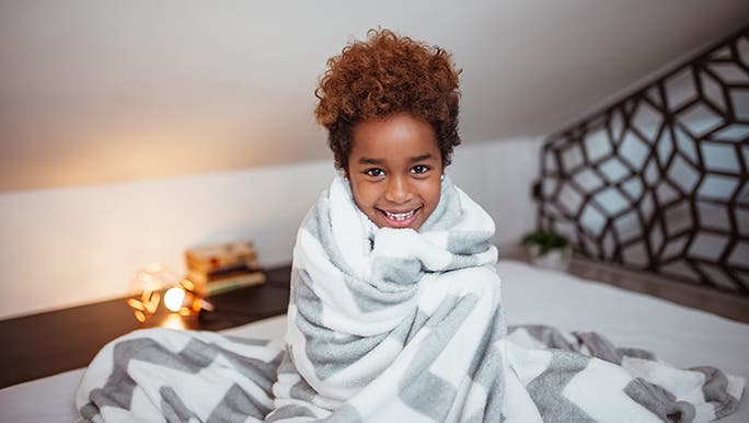 A little boy is wrapped up in a weighted blanket, he is smiling and cosy looking. 