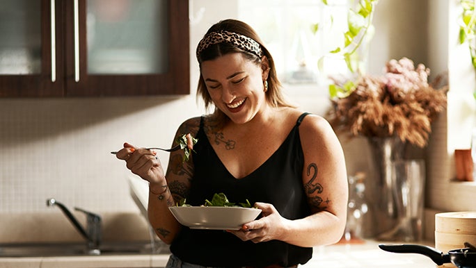 A woman is looking down at the bowl of leafy greens she is eating and is happy because she has made small improvements to her diet which may be able to help her improve gut health naturally.
