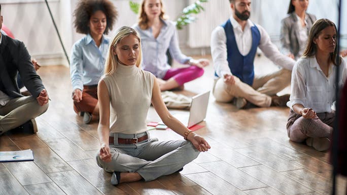  A group of office workers is sitting on the floor practising mindfulness