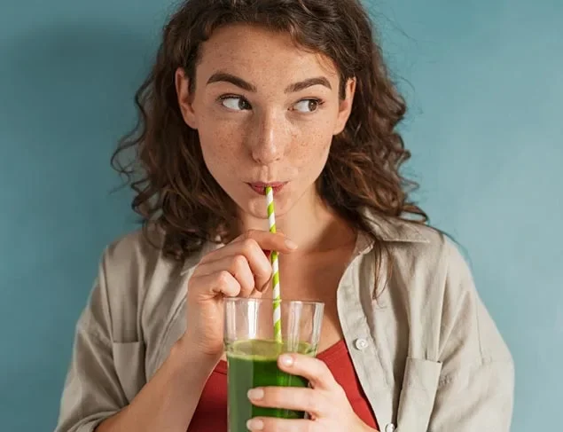 Young woman drinking a green juice through a green and white paper straw