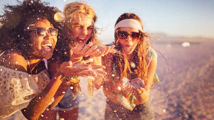 Three happy female friends at the beach throwing sand like it's confetti