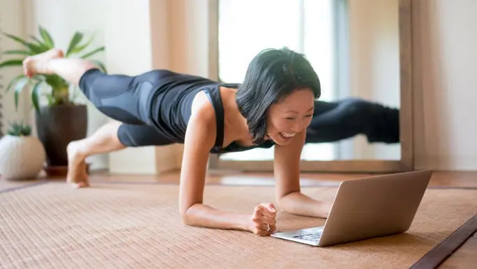 Laughing woman in a plank position at home doing an online workout