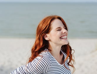 Woman with long red hair on the beach smiling with her eyes shut