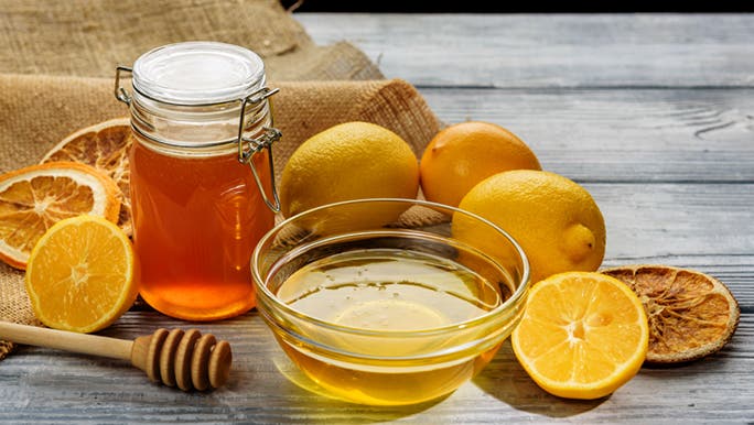 On a wooden table, there are a variety of lemons and honey for skin care.