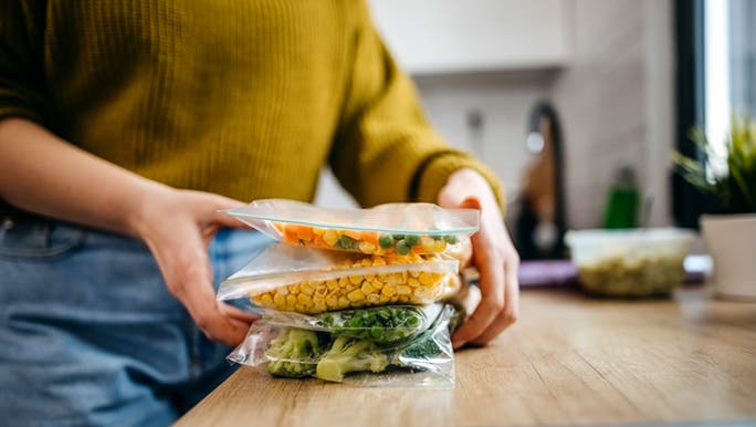 A close up of a woman storing vegetables in ziploc bags. 