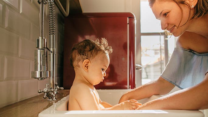 A woman baths a baby in a kitchen sink.