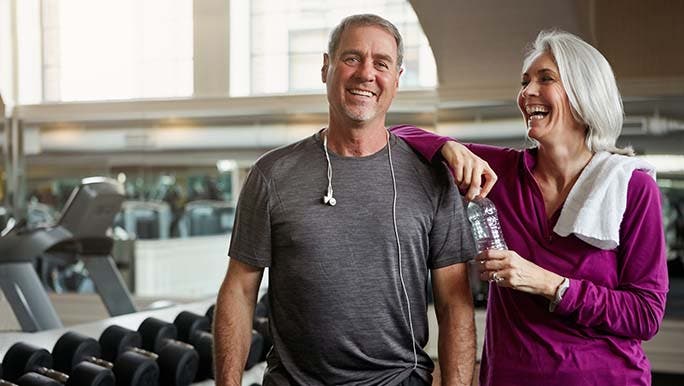 Two people in exercise clothes are at the gym smiling as they’ve just worked out how to get back into going to the gym.