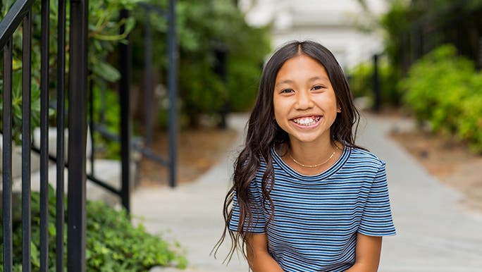 A teenage girl sits on some outside steps and smiles at the camera. 