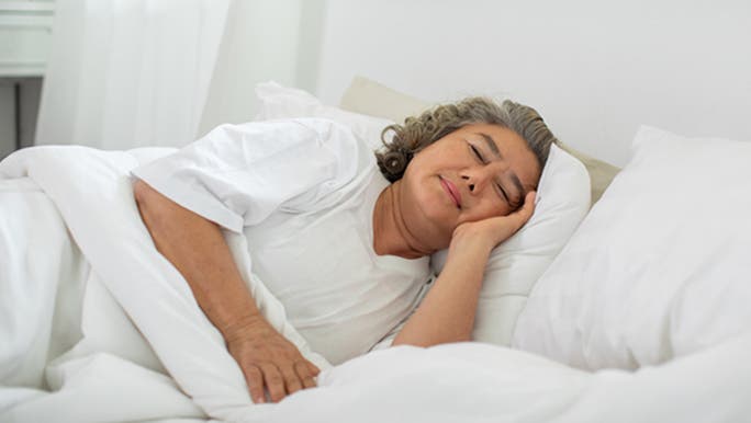 An elderly Asian woman is sleeping in a bed made with white linen