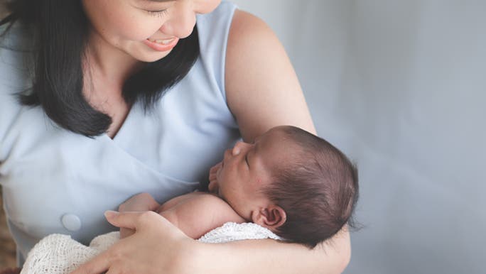 Smiling while holding her child, a mother thinks about why her newborn baby hiccups a lot. 
