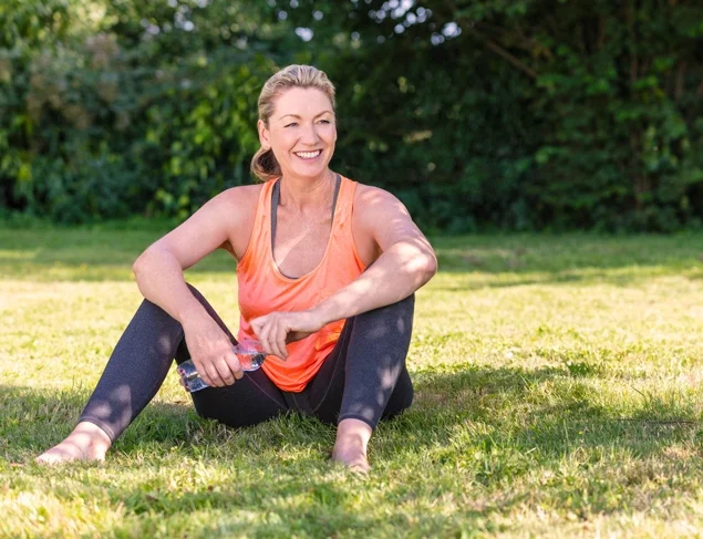 Blonde woman in activewear smiling and sitting in the shade in the park