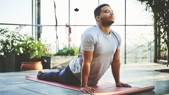 On an outdoor terrace, a man stretches on his yoga mat as a task of his self care checklist.