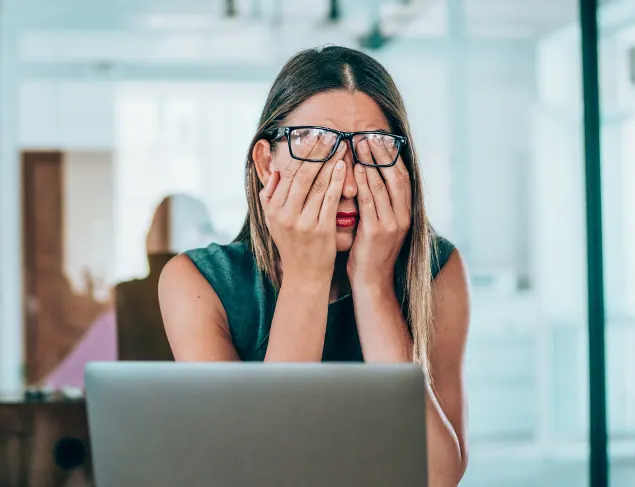 Woman has her head in her hands at work while she sits in front of her laptop experiencing work-related stress.