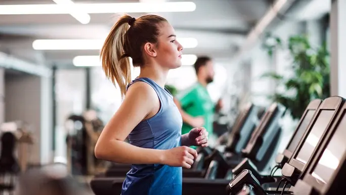 Woman in blue active wear running on the treadmill in the gym