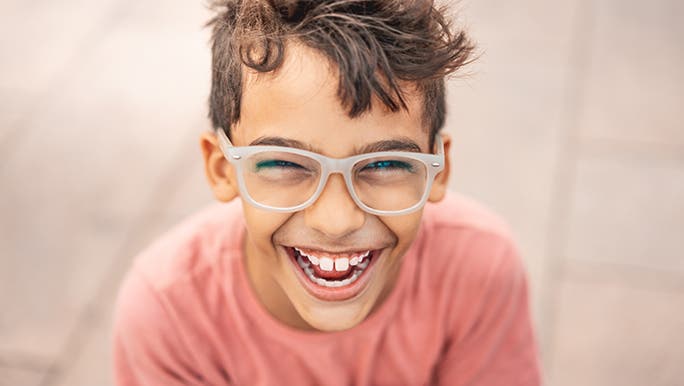 A young teenager smiles straight into the camera which is looking down on him. He looks excited and happy.