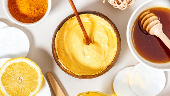 A flat lay image of a turmeric face mask in a bowl surrounded by skincare ingredients