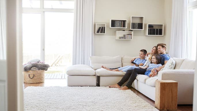 A family sits together on a couch in a minimal, tidy decluttered house. 