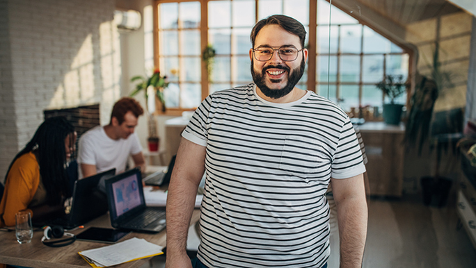 A man with belly fat and wearing a striped T-shirt is smiling at the camera