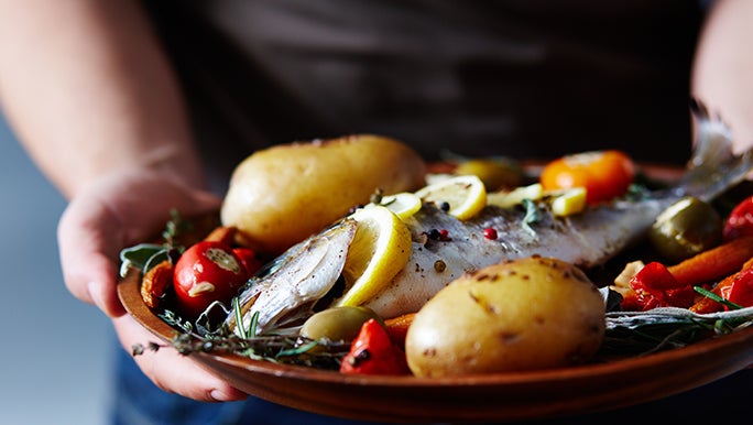 Up close, a man holds a plate of fish and vegetables. These foods are full of vitamins that may help boost your immune system.