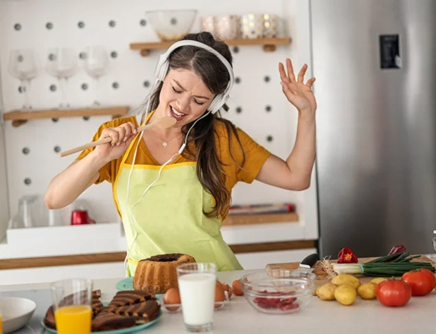 Young woman dressed in yellow and listening to music through headphones having fun in the kitchen