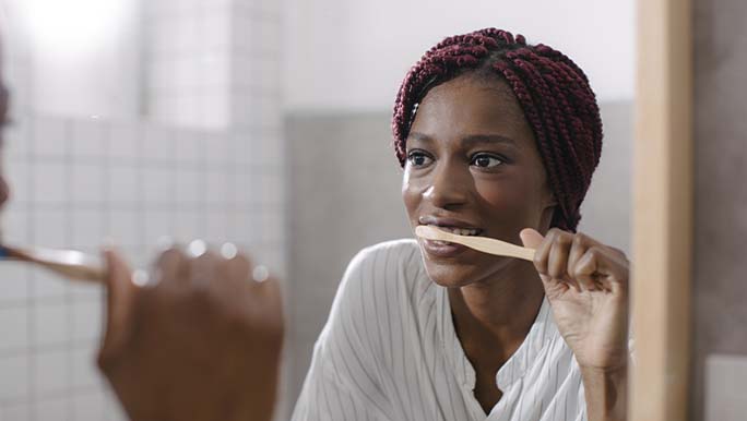 Woman looking in the mirror while cleaning her teeth with natural toothpaste in Australia.