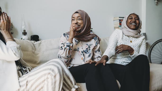 Three women sitting on a couch together laughing. It looks as though they are building a lasting friendship. 