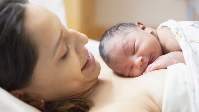 A mother looks down at her newborn baby on her chest and is thinking about whether hiccups are normal in newborn babies. 
