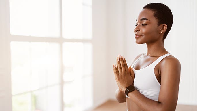 A woman in white activewear meditates after reading the connection between cortisol and mindfulness for stress.
