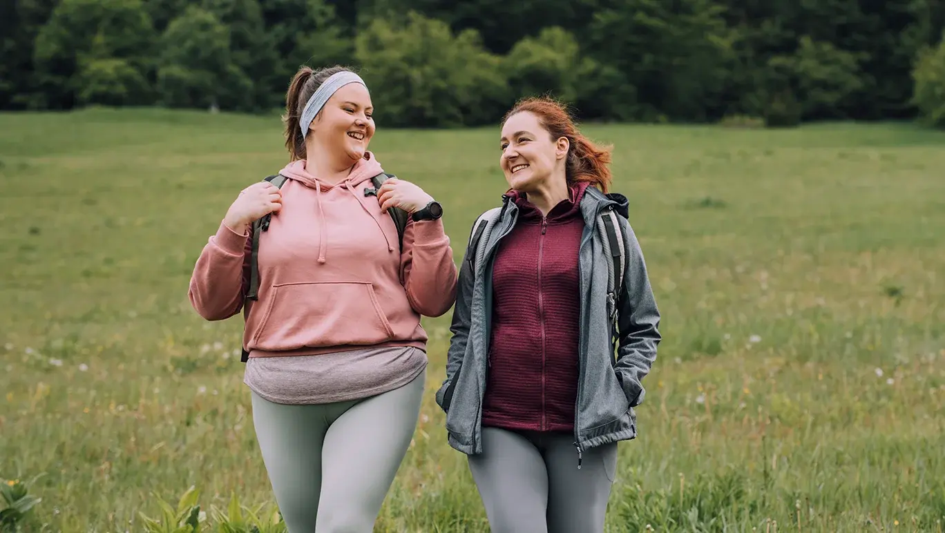 Two friends walk side-by-side as they hike in exercise gear.