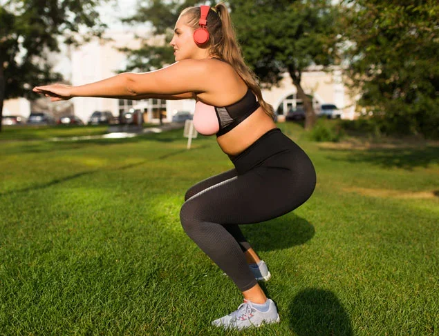 Blonde woman in active wear and pink headphones doing squats in the park