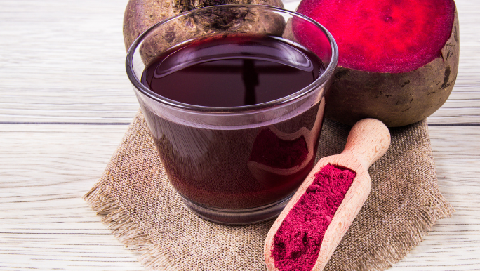 A display of beetroot juice, fresh beetroot vegetables and beetroot powder in a scoop sitting on a timber table