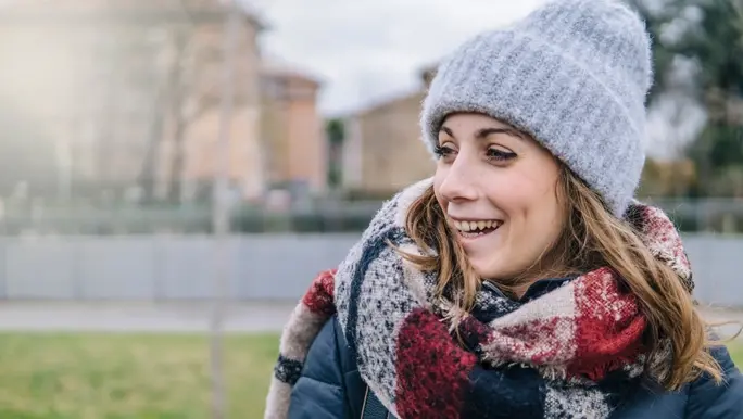 Woman smiling outdoors in winter dressed in a black puffer jacket, woollen scarf and beanie