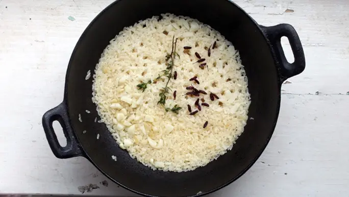 Black cast iron dish with rice, garlic and thyme