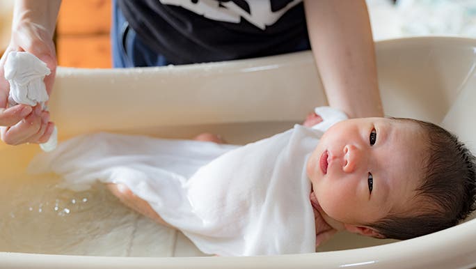 A newborn in a bath is looking straight into the camera. 