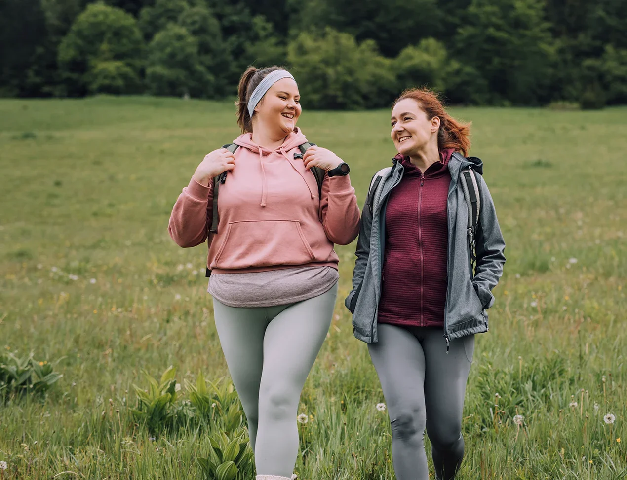 Two friends walk side-by-side as they hike in exercise gear.