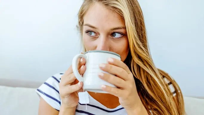 Woman with blonde hair in a white and blue striped t-shirt sipping chamomile tea