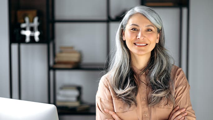 A woman, who is in the process of transitioning to grey hair with highlights, smiles into the camera