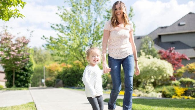 A young mother is walking with her young daughter in a suburban neighbourhood while holding hands