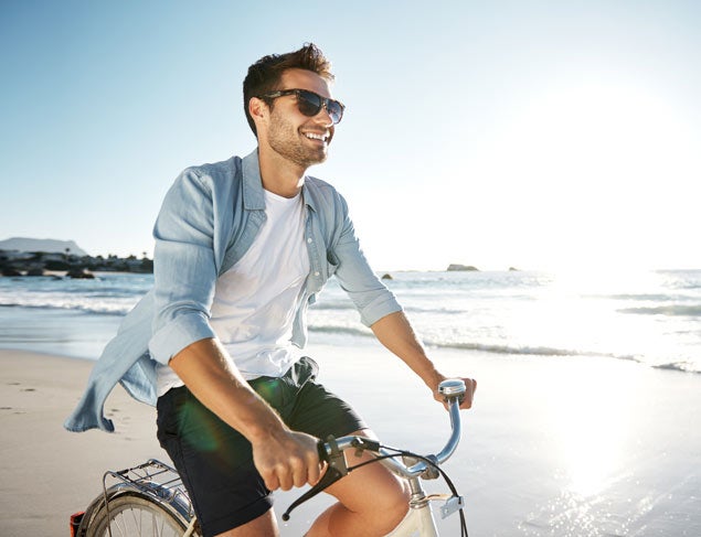Smiling man enjoying the sun riding a bike at the beach