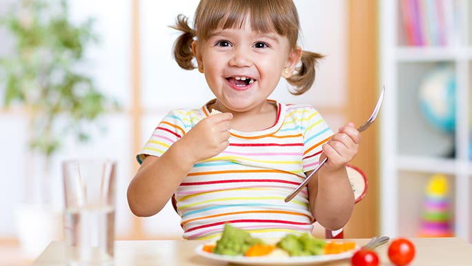 A girl with a fork-in-hand is happily eating some vegetables which is part of her daily fruit and vegetable nutrition. 