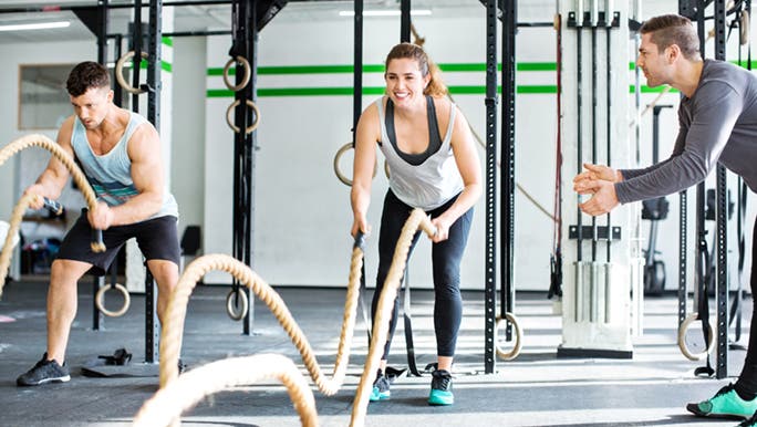 Two young people are enjoying a functional training system in a gym, supported by their trainer.