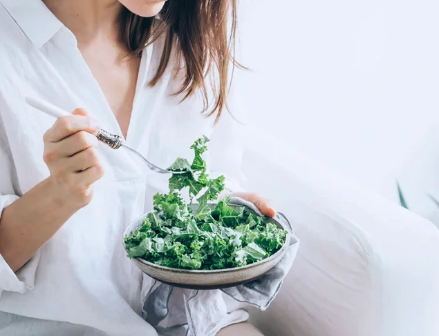 Woman in a white shirt eating a kale salad