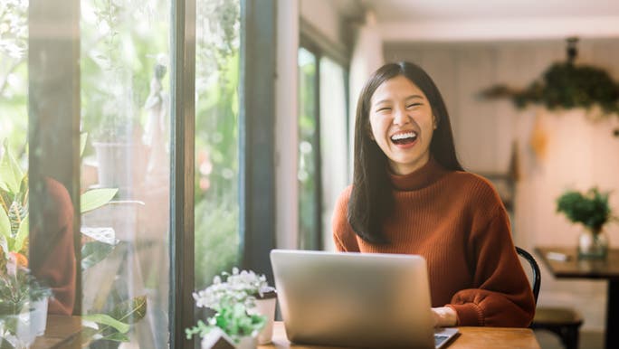 While working on her laptop, a woman is smiling because she knows how to prioritise tasks. 